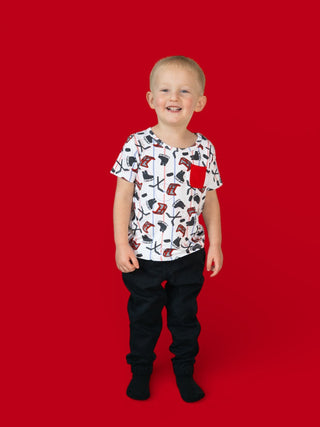 Child wearing white short-sleeve tee with red and black skateboard and hockey stick print and black pants against red backgro