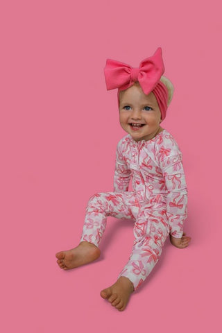 Toddler wearing pink checkered romper with bow headband against pink background.