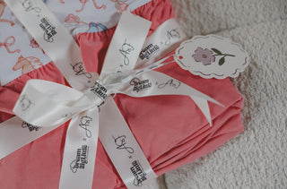 Pink and white ruffle blanket with floral print, tied with branded white ribbon and matching gift tag.