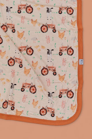 Cream blanket with red tractors, chickens, cows, pigs, and grass pattern, orange binding on edges.