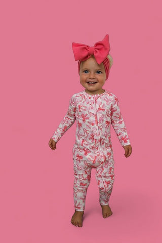 Toddler wearing pink bow headband and pink checkered bow-print long-sleeve romper against pink background.