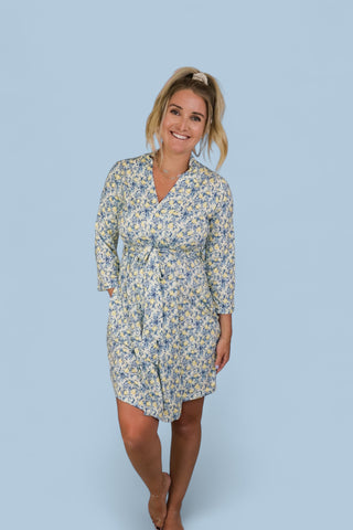 Woman wearing a knee-length robe with blue and yellow floral toile print, three-quarter sleeves, and a wrap-front closure.