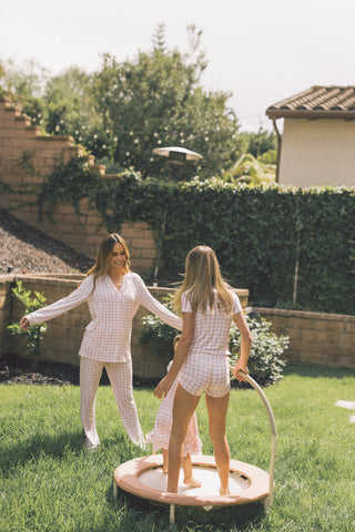 Two women wearing pink and white gingham pajama sets in a backyard setting.