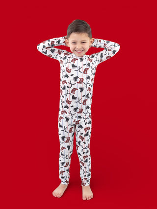 Child wearing white long-sleeved pajamas with red and black hockey stick and skate pattern on red background.