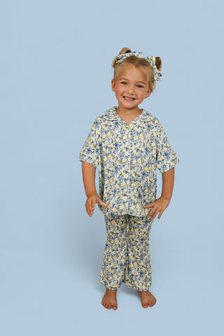 Girl wearing yellow and blue citrus toile print button-up shirt and matching flare pants with matching hair bows.