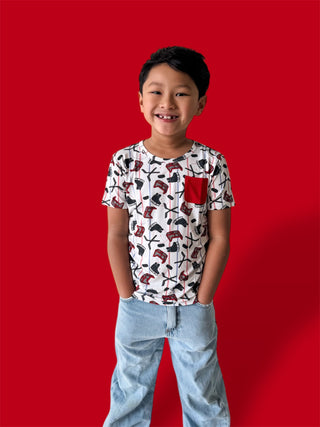 Boy wearing white short-sleeve tee with red hockey stick and skateboard print, red chest pocket, paired with light blue jeans