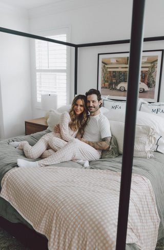 Woman wearing pink and white gingham pajama set with flare pants, sitting on bed with man.