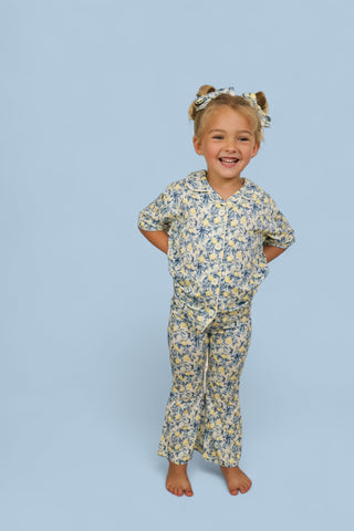 Young girl wearing cream and blue toile print short-sleeve top and flared pants with matching hair bow.