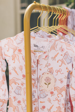 White romper with orange floral and boot print pattern hanging on gold hangers.