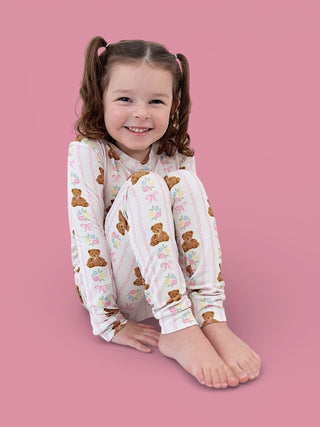 Toddler wearing long-sleeve pajamas with bear and floral print on pink background.