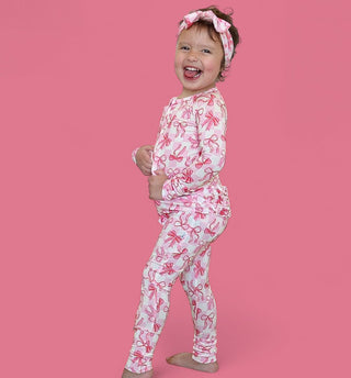 Toddler wearing white romper with pink bow print, long sleeves, and ruffled legs, paired with matching pink bow headband.
