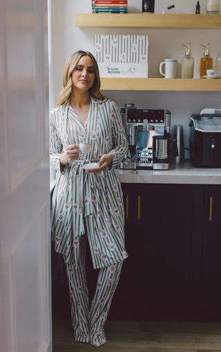 Woman wearing gray and white striped robe with pink floral print, holding a cup in a kitchen.