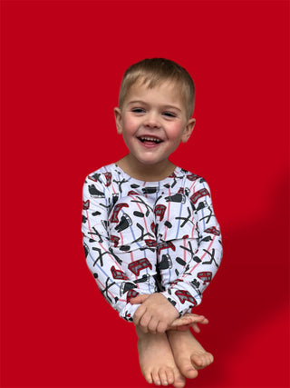 Young child wearing white long-sleeve pajamas with hockey stick and skate print pattern against red background.