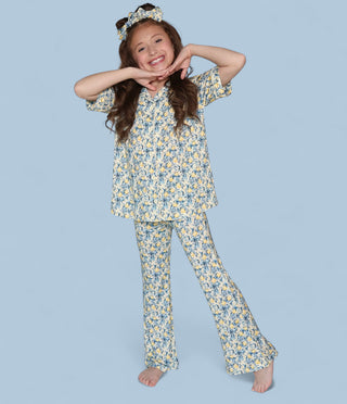Girl wearing yellow and blue citrus toile print short-sleeve shirt and matching flare pants with coordinating headband.