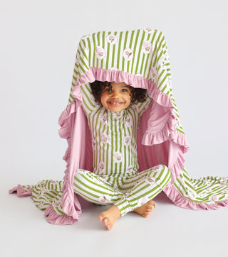 Toddler wearing green and white striped pajamas with pink floral print, wrapped in matching pink ruffled blanket.