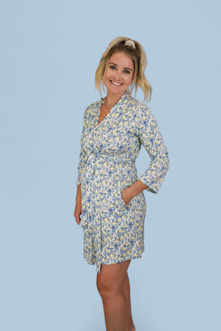 Woman wearing a cream and blue toile patterned wrap robe with three-quarter sleeves and side pockets.