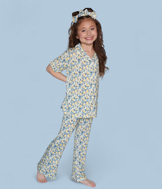 Girl wearing a yellow and blue citrus toile print shirt and flare pants set with matching headband.