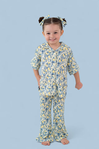 Young girl wearing yellow and blue citrus toile print pajama set with puffed sleeves and flared pants, paired with matching h