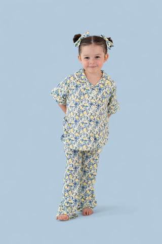 Girl wearing yellow and blue citrus toile print button-up shirt and matching flared pants with coordinating hair bows.