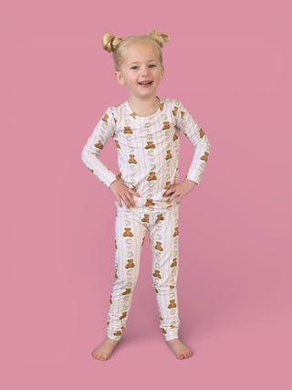 Young child wearing cream-colored long-sleeve pajamas with brown bears and floral print throughout, standing against a pink b