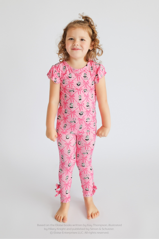 Girl wearing pink sleep pants with ribbon and ballet shoe print, short sleeves, ruffle trim at ankles.