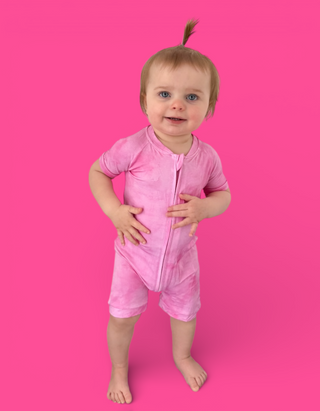Toddler wearing pink short-sleeved romper with front zipper against bright pink background.