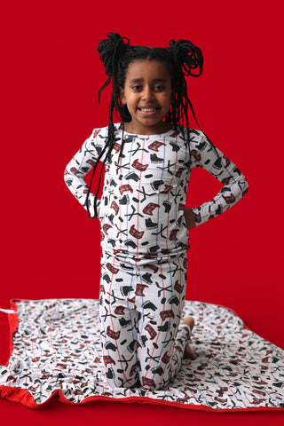 Child wearing white long-sleeve pajamas with black and red skate and stick print pattern against red background.