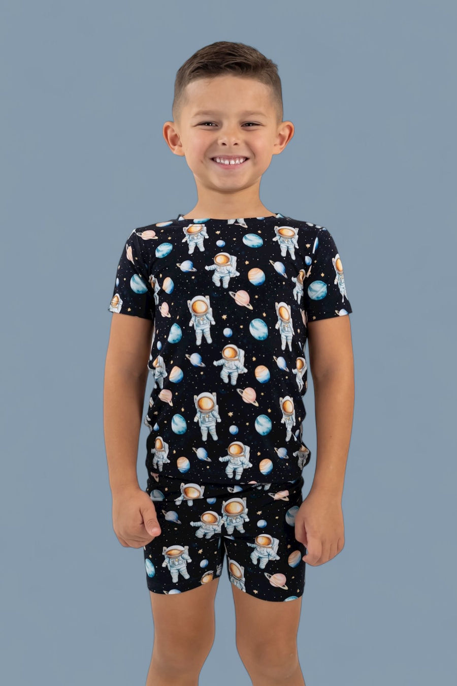 Boy's short pajama set with black shirt and shorts featuring astronauts and planets pattern.
