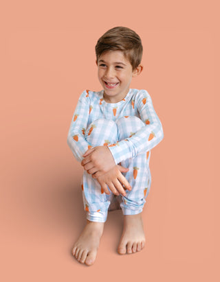 Child wearing blue and white checkered pajamas with orange carrot pattern, long sleeves and cropped legs.