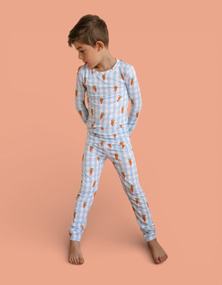 Child wearing light blue gingham pajama set with carrot pattern on long-sleeve top and matching pants.