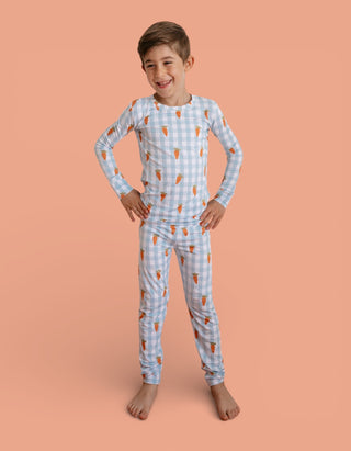 Child wearing light blue gingham pajama set with orange carrot print throughout, featuring long sleeves and full-length pants