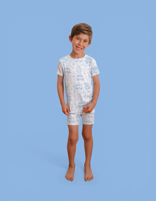 Boy wearing blue and white toile print short-sleeve shirt and matching shorts against blue background.