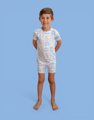 Boy wearing blue and white toile print short-sleeved shirt and matching shorts against blue background.