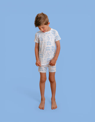 Child wearing cream short-sleeved shirt and shorts with blue toile pattern featuring pastoral design elements.
