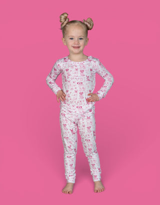 Young child wearing white long-sleeve pajamas with pink puppy toile print pattern against pink background.