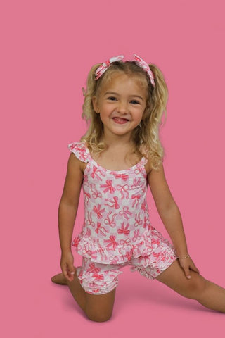 Young girl wearing pink and white bow-print ruffle shorts with matching sleeveless top and coordinating hair bows.