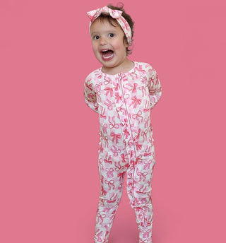 Toddler wearing pink and white bow-print romper with matching headbow against pink background.