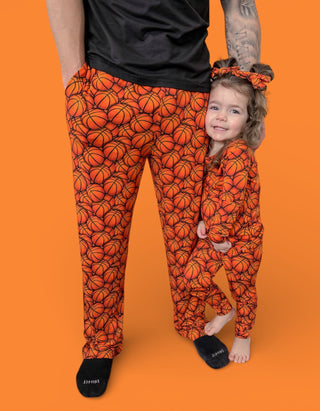 Adult and child wearing matching orange pajama sets with basketball print, black socks, and coordinating hair scrunchies agai
