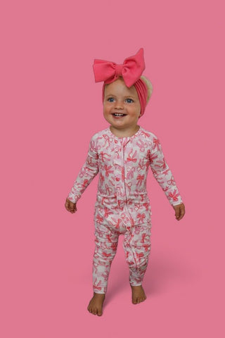 Toddler wearing pink bow headband and long-sleeve romper with pink bow pattern on cream background.