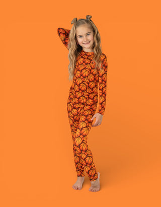 Child wearing orange long-sleeve pajamas with basketball pattern and matching hair clips against orange background.