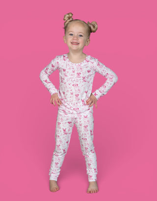 Young child wearing a two-piece pajama set with pink and white toile puppy print, long sleeves and full-length pants.