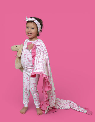 Toddler wearing pink and white puppy-print pajamas with matching headband, holding stuffed dog toy.