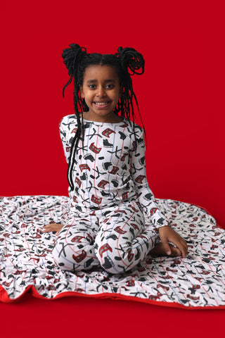 Child wearing white pajamas with hockey stick and skate print on red background.