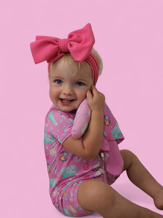 Pink plush lovey with textured bow held by smiling toddler wearing matching patterned outfit.
