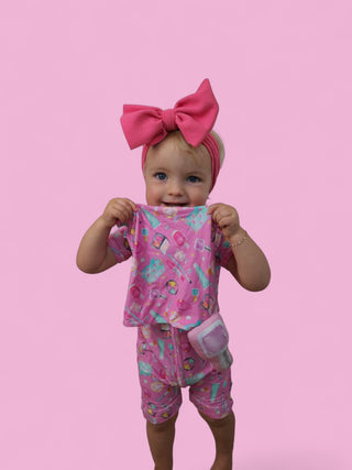 Toddler wearing pink plush two-piece set with geometric pattern and matching pink bow headband.