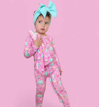 Toddler wearing pink pajamas with colorful print and turquoise bow headband, holding pink plush toy against chest.