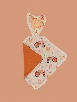 Soft plush lovey with hen-shaped head, cream fabric printed with farm animals and tractors, orange backing.