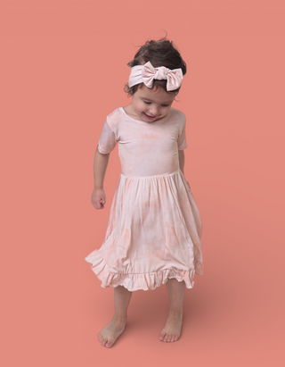Toddler wearing pale pink bow headband with matching short-sleeved dress and ruffled hem.