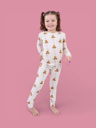 Young child wearing white long-sleeve pajama set with brown teddy bears and pink flowers on pink background.