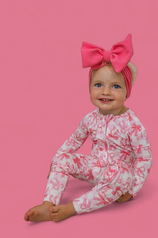 Toddler wearing pink and white bow-print romper with long sleeves and matching pink bow headband.